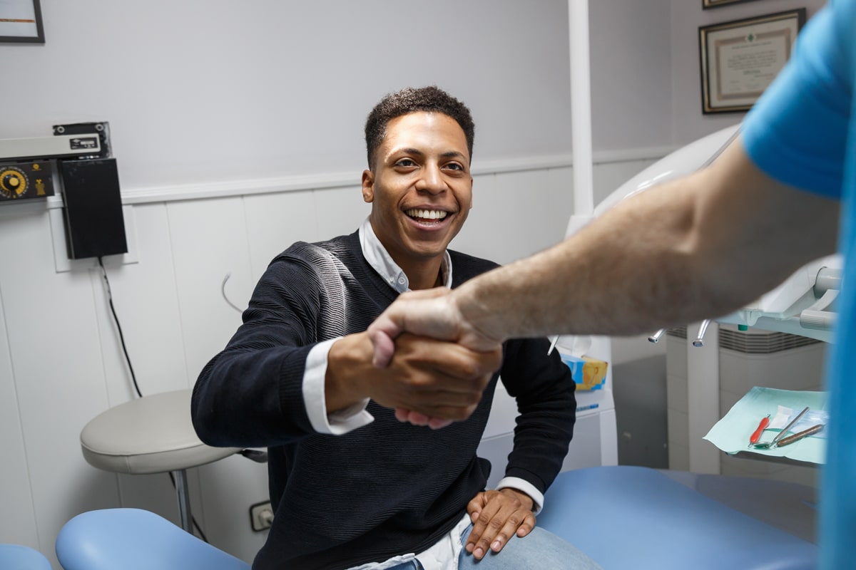 A smiling man in a medical office shakes hands with a healthcare professional. Medical tools and certificates are in the background.